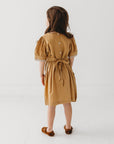 Back view of a girl wearing the mustard puff sleeve dress with a waist tie.