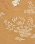Close-up of light-colored floral embroidery across the mustard dress yoke.