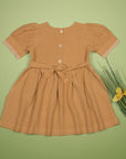 Back of the mustard dress arranged flat, showing button closures and a tied waist bow.