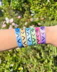 Highs and Lows tie-dye bracelet set worn together on a wrist outdoors against green foliage