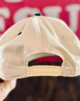 Beige cap held by a hand with a blurred background featuring text.