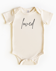 Baby wearing “Loved” affirmation bodysuit – Christian script design organic cotton outfit by Lumiere Vive
