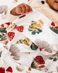 Baby wrapped in a blanket with a forest-themed pattern, surrounded by Christmas decorations.