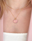 Necklace with a pink pendant featuring initials on a person wearing a light pink top.