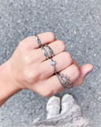 Silver-tone cross promise ring styled with other rings on a hand outdoors