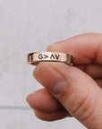 Rose gold ring with engraved symbols held by a hand against a light background