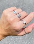 Hand wearing multiple silver rings on a gray pavement background