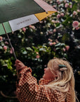 Person holding a green umbrella with a visible brand logo, standing in front of a floral background.