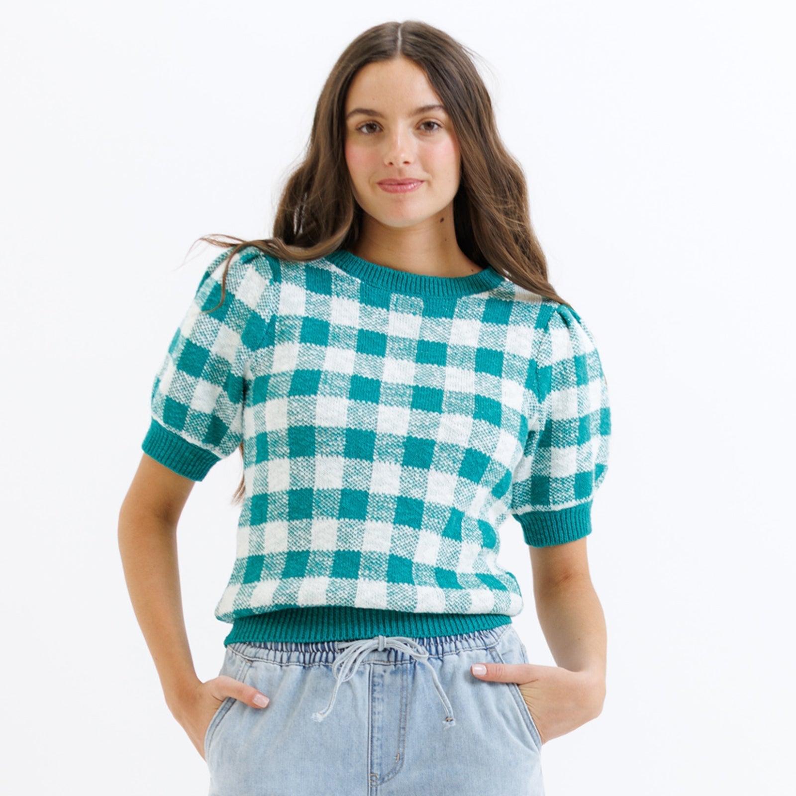 Woman wearing a green and white checkered sweater with light blue jeans on a white background