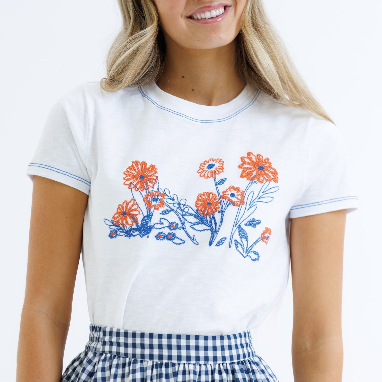 Woman wearing a white t-shirt with floral designs on a plain background