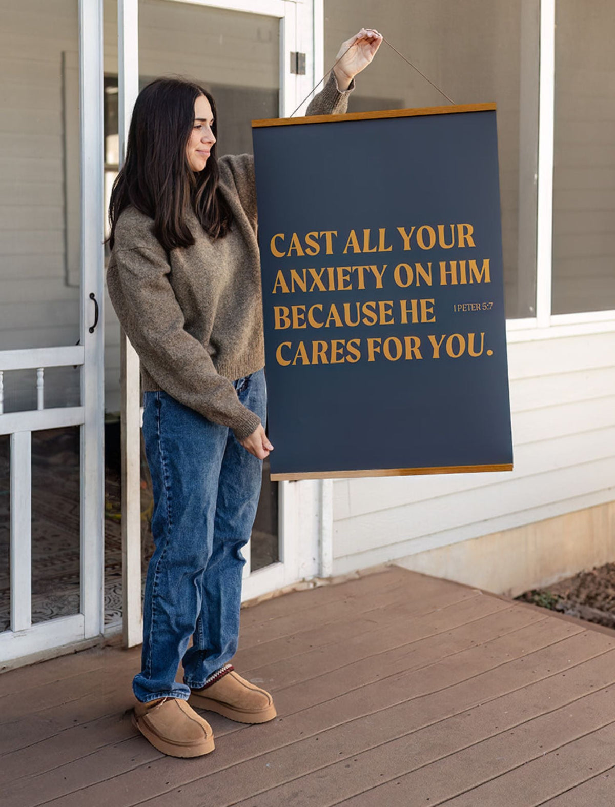Woman holding the Cast All Your Anxiety 24 x 36 scripture poster with golden lettering on a deep blue background.