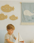 Child playing with a wooden boat in a room with whale decorations and Lullaby Rattan branding.