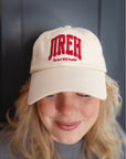 Close view of a light neutral dad hat with red Jireh and The Lord Will Provide embroidery