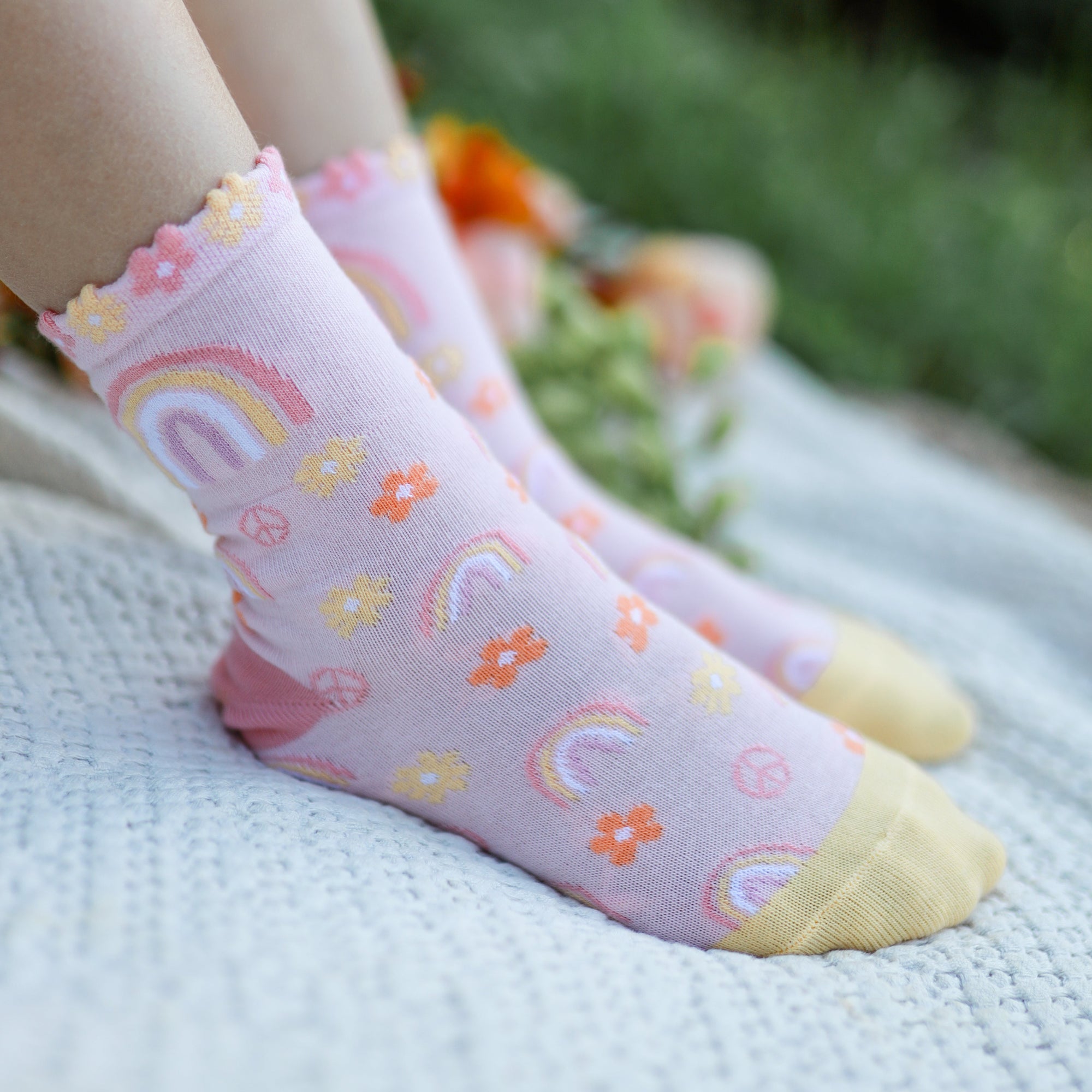 Pink socks with colorful patterns worn by a person sitting on grass.
