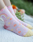 Pink socks with colorful patterns worn by a person sitting on grass.
