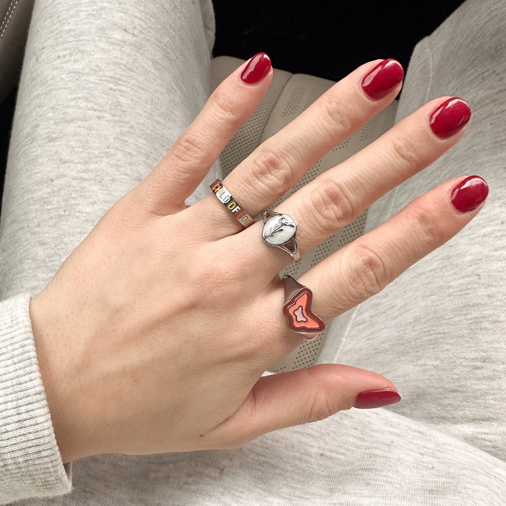 Hand with red nail polish wearing multiple rings on a neutral background