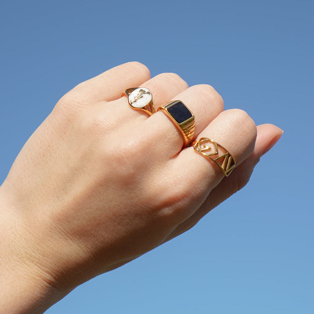 Hand wearing three gold rings against a clear blue sky