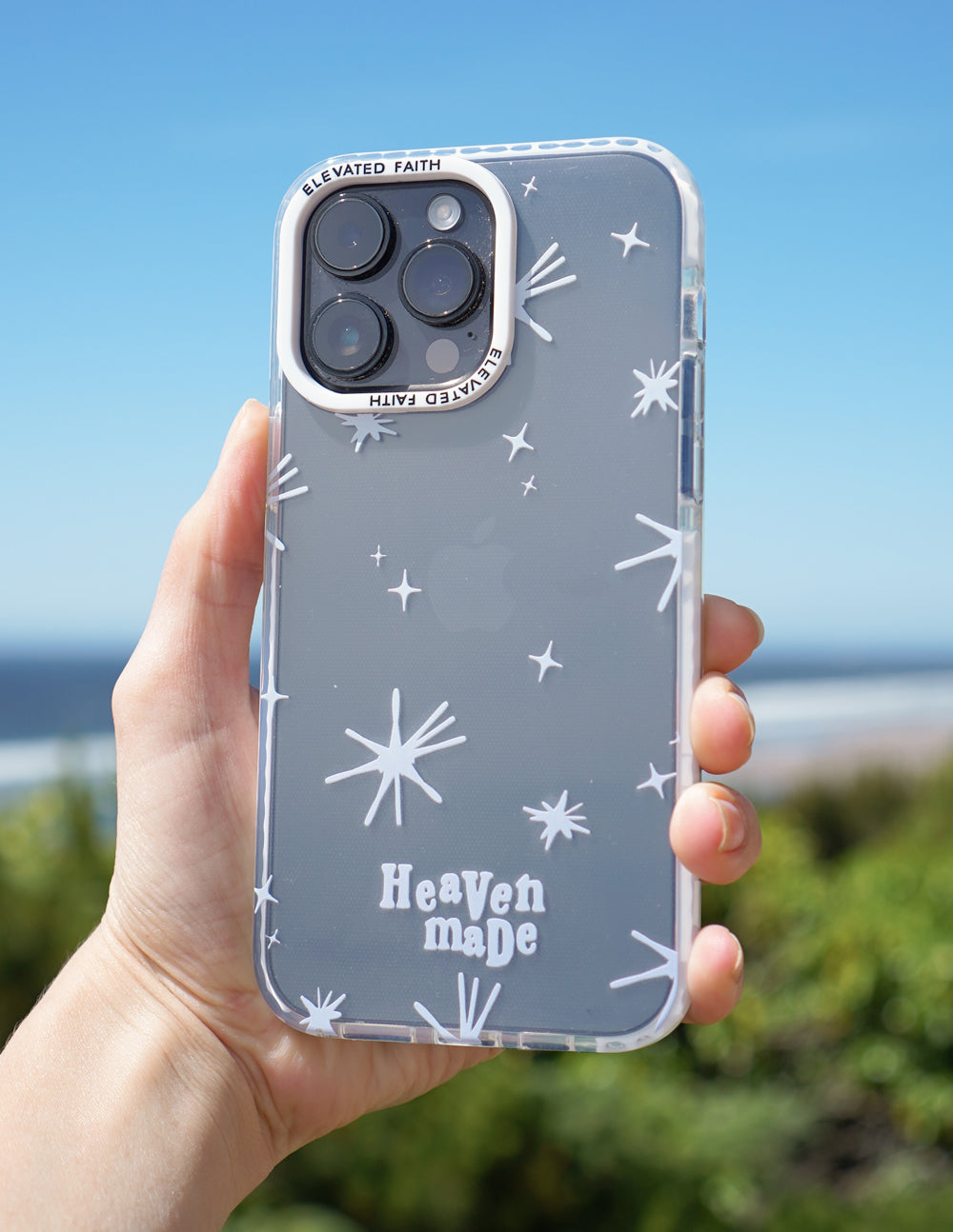 Heaven Made starburst iPhone case held outdoors against a blue sky and green landscape