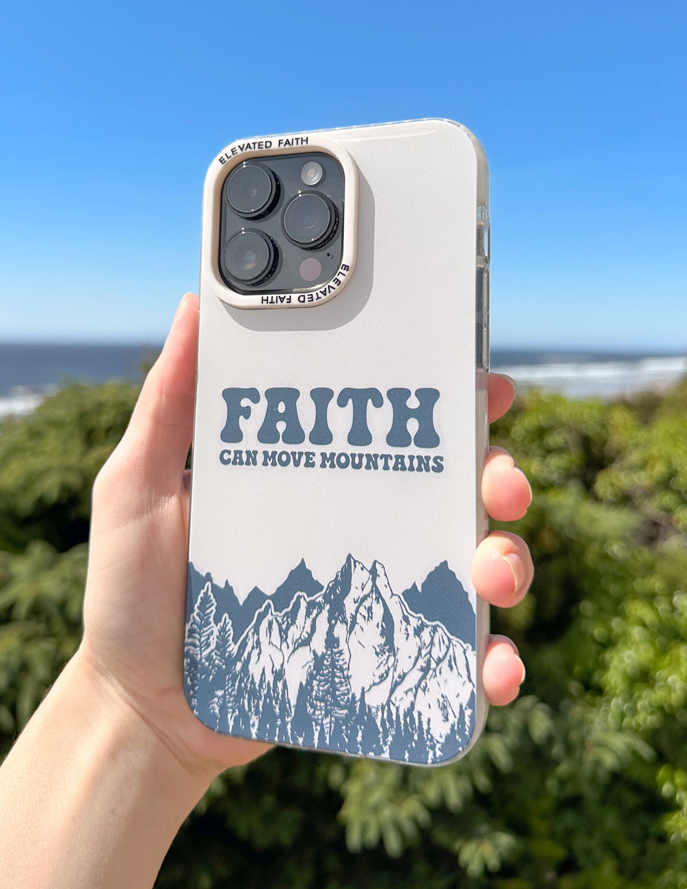 Faith Can Move Mountains iPhone case held outdoors with greenery and blue sky in the background