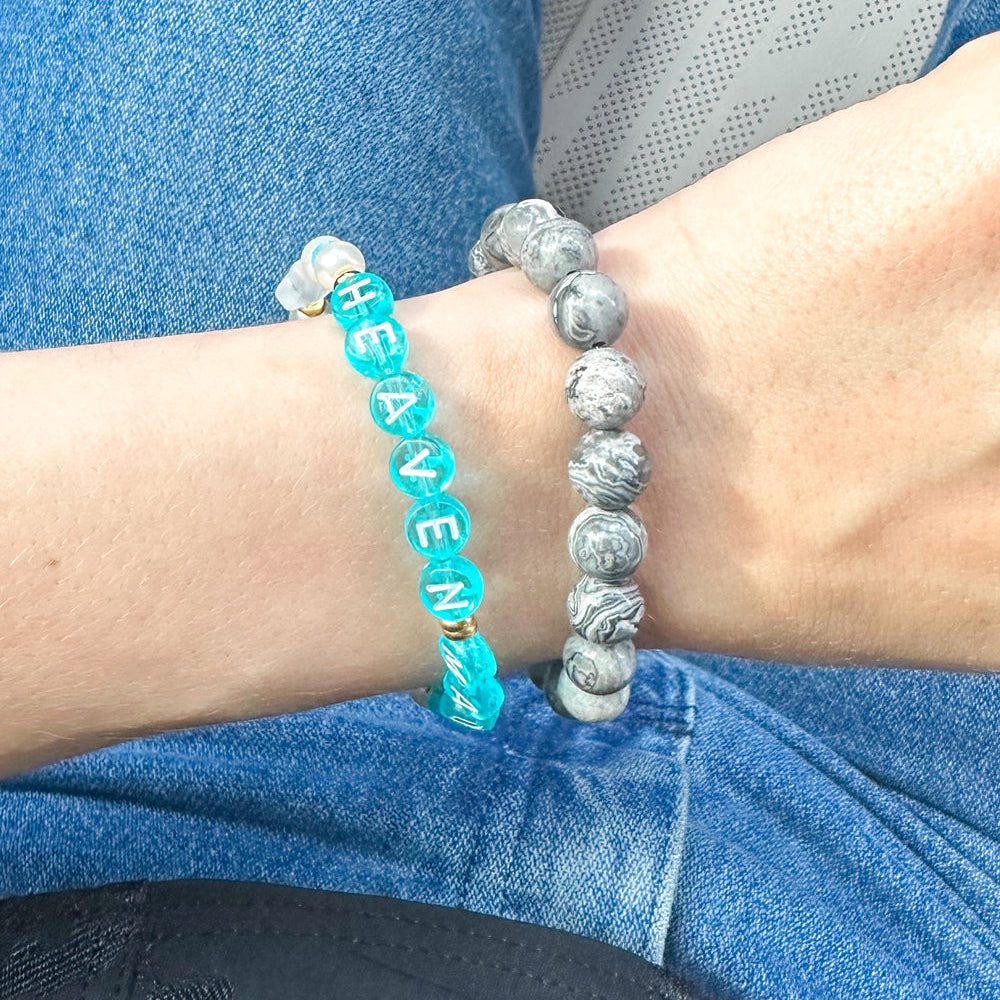 Close-up of a wrist wearing two bracelets with 'HEAVEN' and 'HEAVENLY' text.