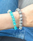 Close-up of a wrist wearing two bracelets with 'HEAVEN' and 'HEAVENLY' text.