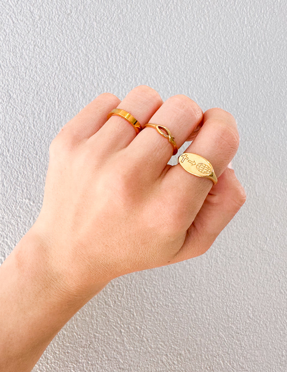 Hand wearing the Jesus Fish Gold-Tone Ring alongside other gold-tone rings against a light textured wall