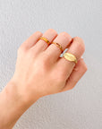 Hand wearing the Jesus Fish Gold-Tone Ring alongside other gold-tone rings against a light textured wall