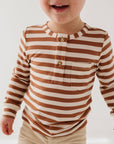 Child wearing a brown and white striped shirt with beige pants on a plain background