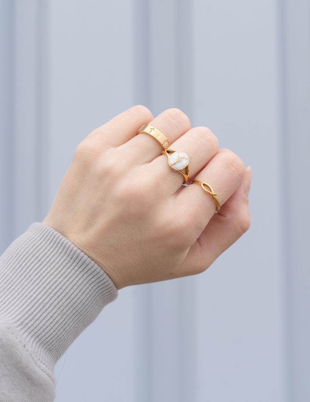 Jesus Fish Gold-Tone Ring styled with other rings on a hand extending from a gray sleeve