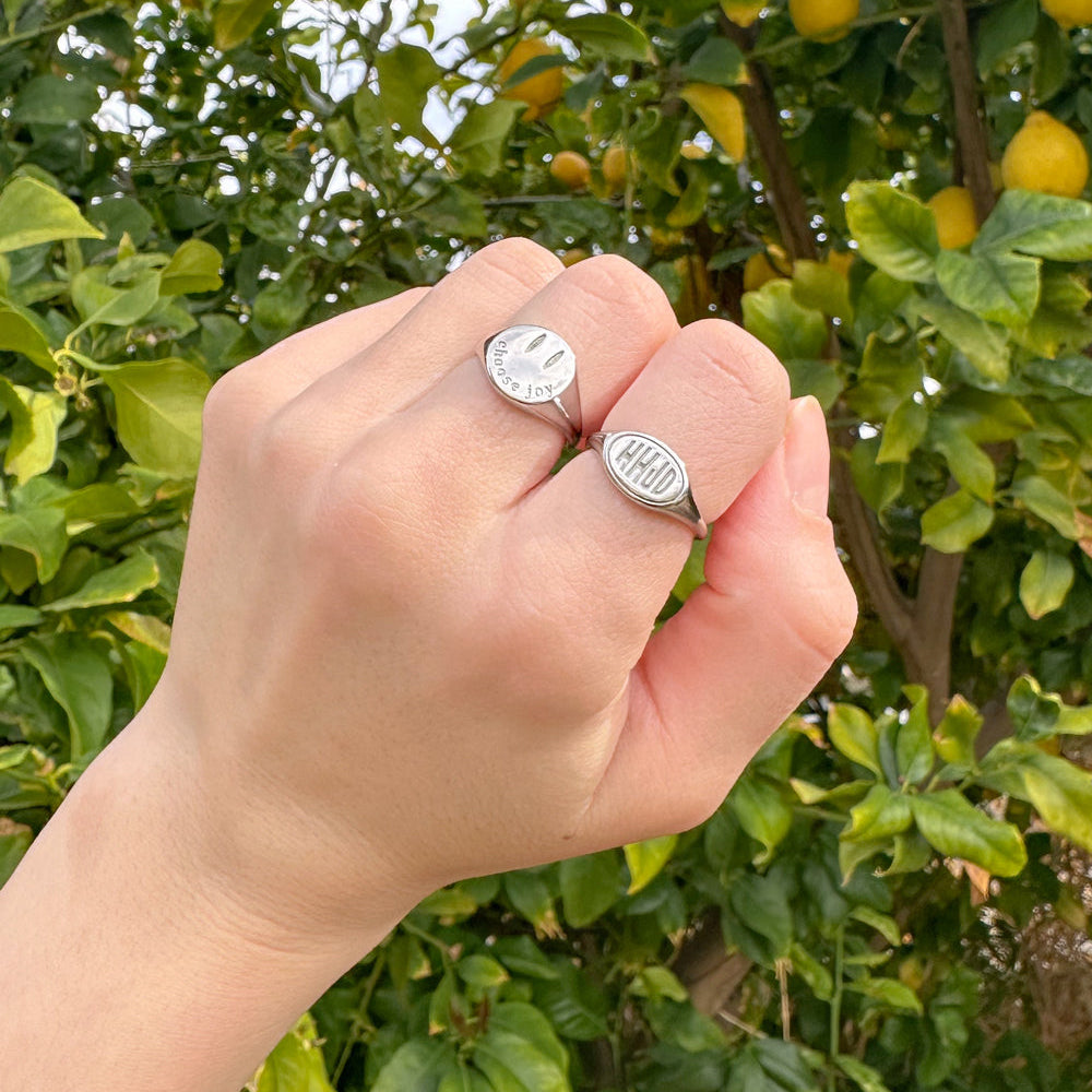 Hand wearing two silver rings with engraved text against a lemon tree background