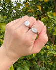 Hand wearing two silver rings with engraved text against a lemon tree background