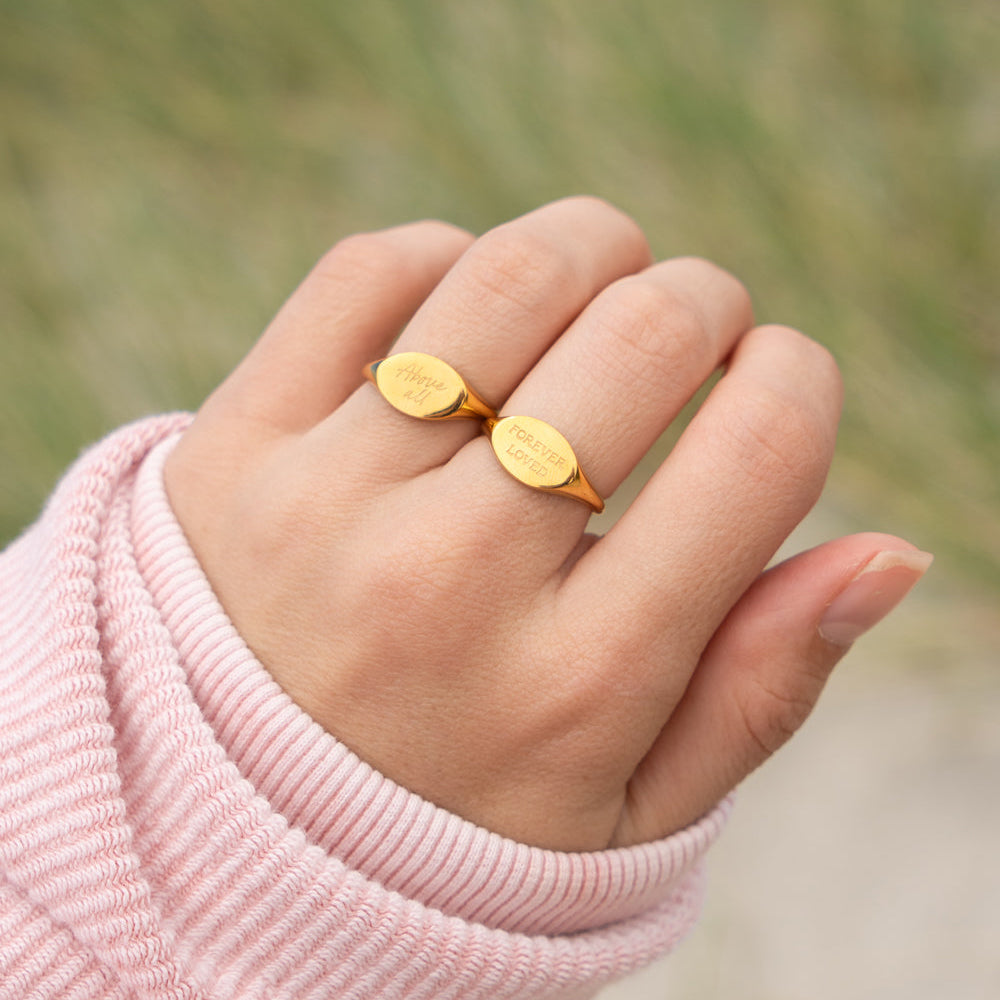 Hand wearing a gold ring with a blurred natural background