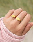 Hand wearing a gold ring with a blurred natural background