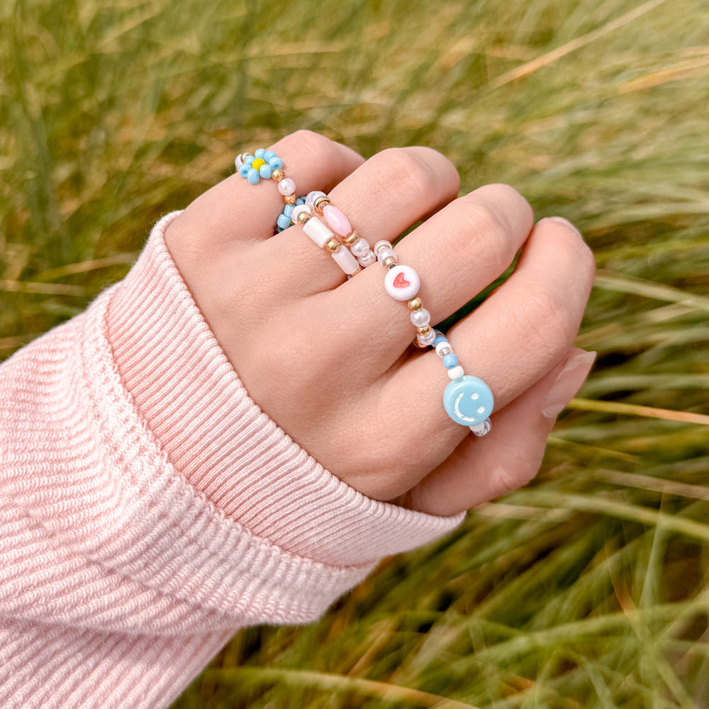 Hand wearing multiple beaded rings with a blurred grass background