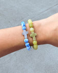 Yellow Restoration Cross bracelet worn beside a separate blue beaded bracelet