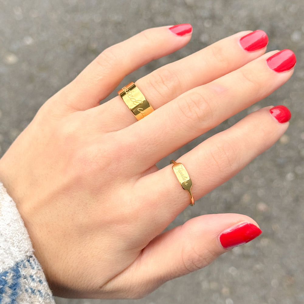 Hand with red nail polish wearing two gold rings on a blurred background