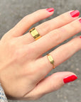 Hand with red nail polish wearing two gold rings on a blurred background
