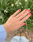 Everlight gold-tone cross bracelet styled with rings and pink nails against garden greenery
