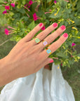 Lilac Enamel Cross Ring styled with other colorful cross rings on a hand beside pink flowers