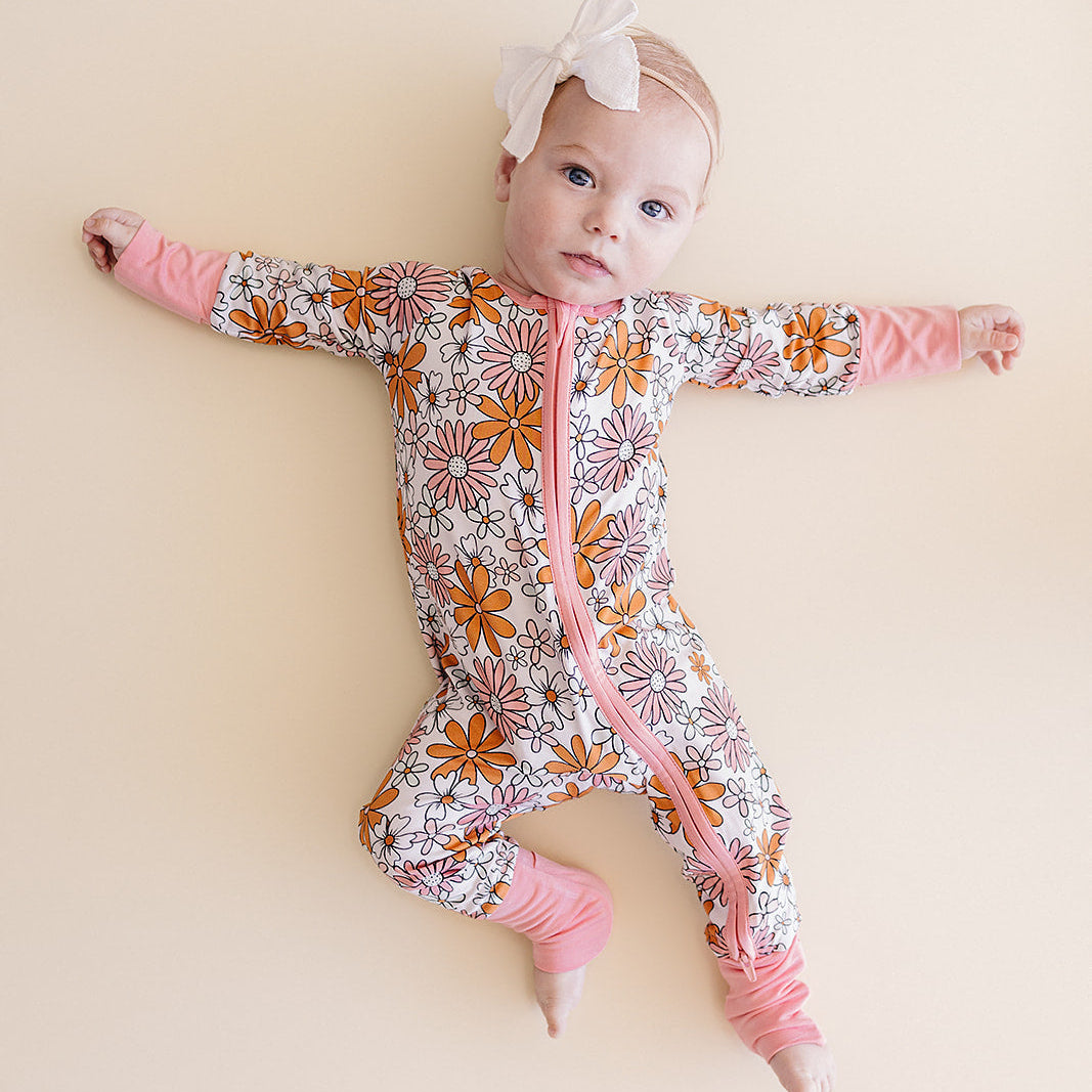 Baby in a floral onesie with pink accents on a beige background