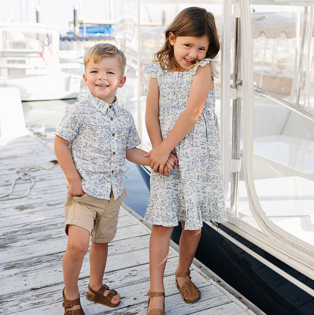 Two children holding hands on a dock with boats in the background