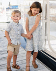 Two children holding hands on a dock with boats in the background