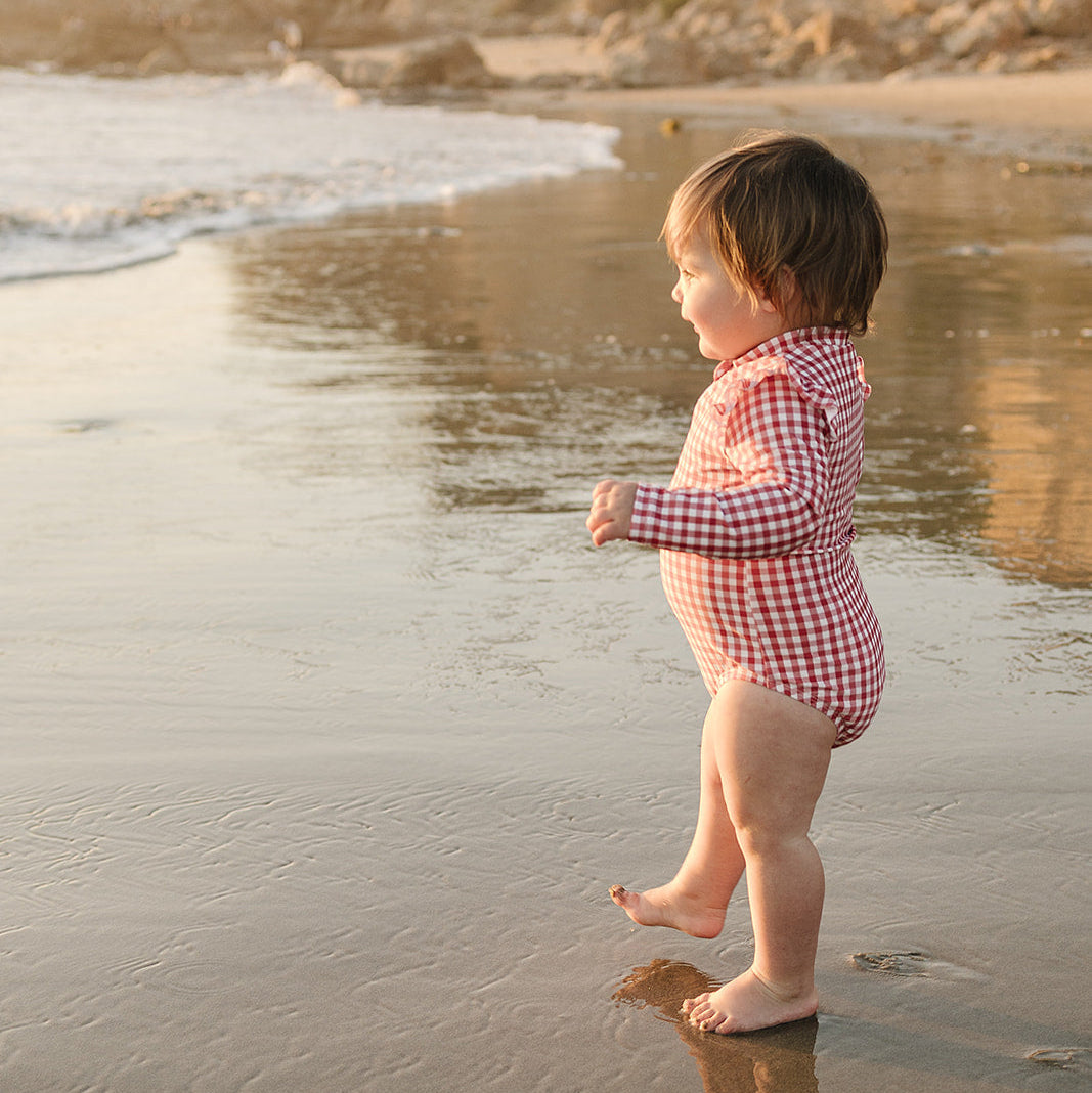 Child in a checkered swimsuit standing on a beach with cliffs in the background