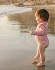 Child in a checkered swimsuit standing on a beach with cliffs in the background