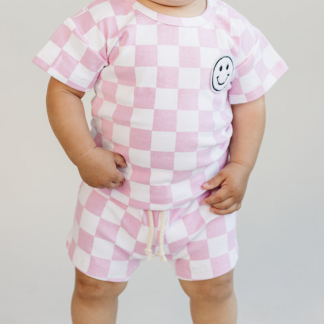 Child wearing a pink and white checkered outfit with a smiley face design on a plain background