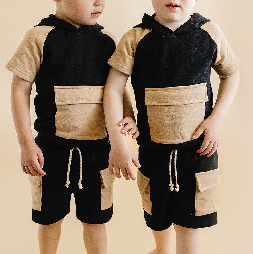 Two young boys wearing matching black and beige outfits on a beige background