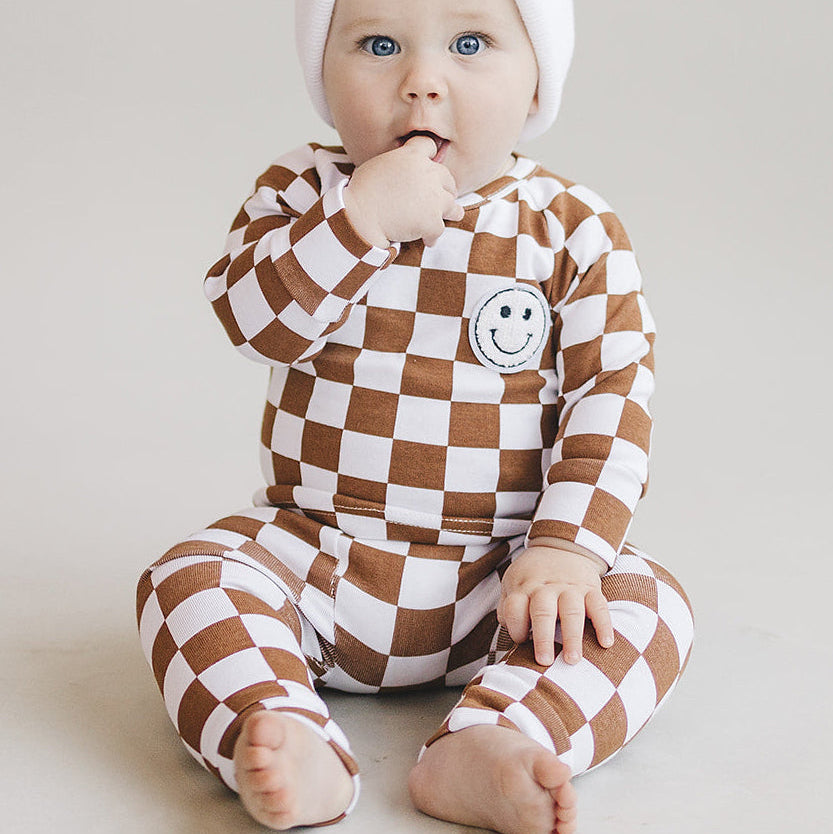 Baby wearing a checkered brown and white outfit with smiley face design on a light gray background