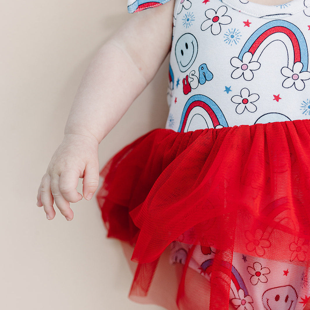 Baby wearing a colorful outfit with a red tutu on a beige background