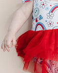 Baby wearing a colorful outfit with a red tutu on a beige background