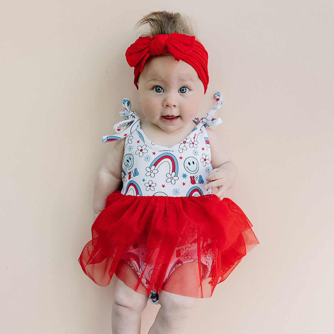 Baby wearing a red dress with a colorful pattern on a beige background